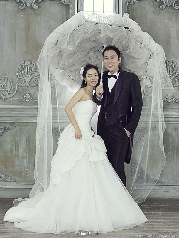 Bride and groom in wedding attire posing under a large tulle parasol umbrella