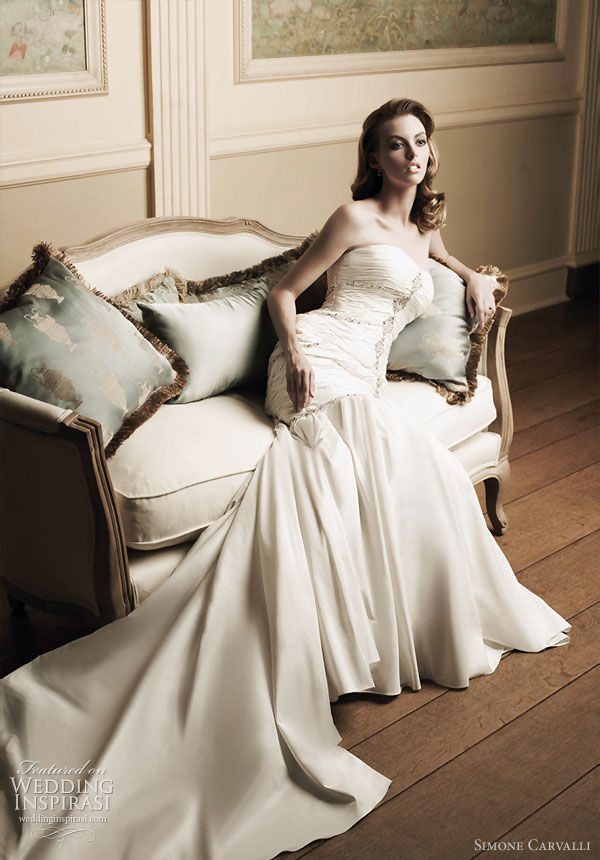 Bride sitting, posing in a wedding dress from Simone Carvalli  bridal gown collection featuring beautiful ruching around the bodice,  soft drape skirt